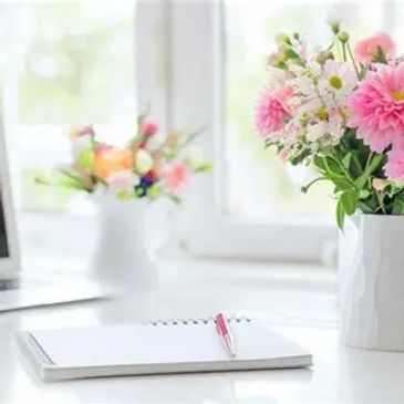 Notepad, pen, vase with flowers, and laptop.