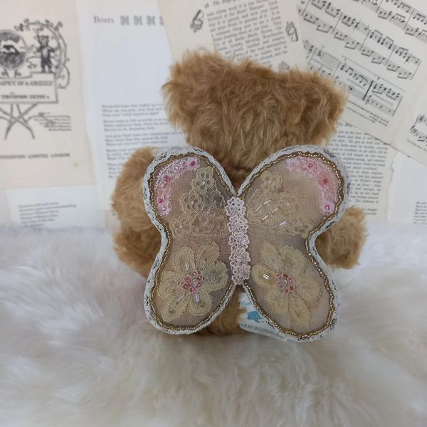 A view of the back of a brown mohair artist teddy bear showing the beaded lace wings attached to it