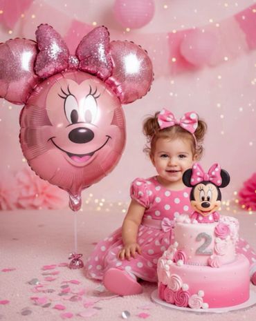 A toddler girl in pink polka dot dress with Minnie Mouse balloon and cake.