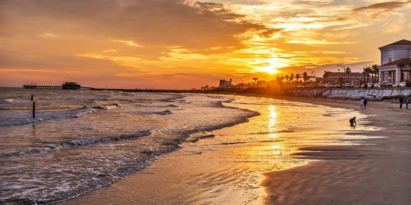 Sunset over a calm beach with gentle waves and a few people walking.