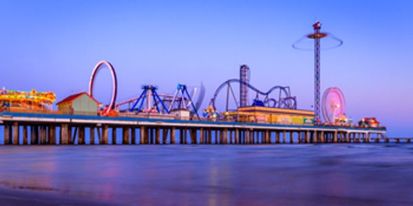 A vibrant amusement park pier with roller coasters and rides at dusk.
