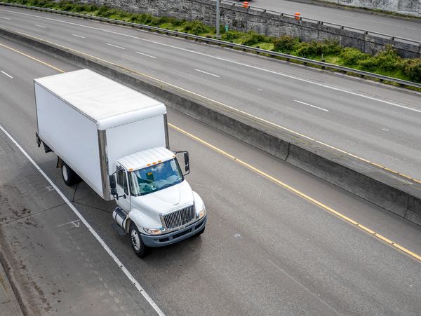 Powerful compact meddle size rig semi truck with box trailer driving on the highway road with exit.