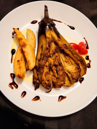 Grilled stuffed eggplant with potato wedges and cherry tomatoes on a white plate.