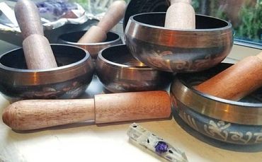 Several Tibetan singing bowls with wooden mallets and a small crystal on a surface.