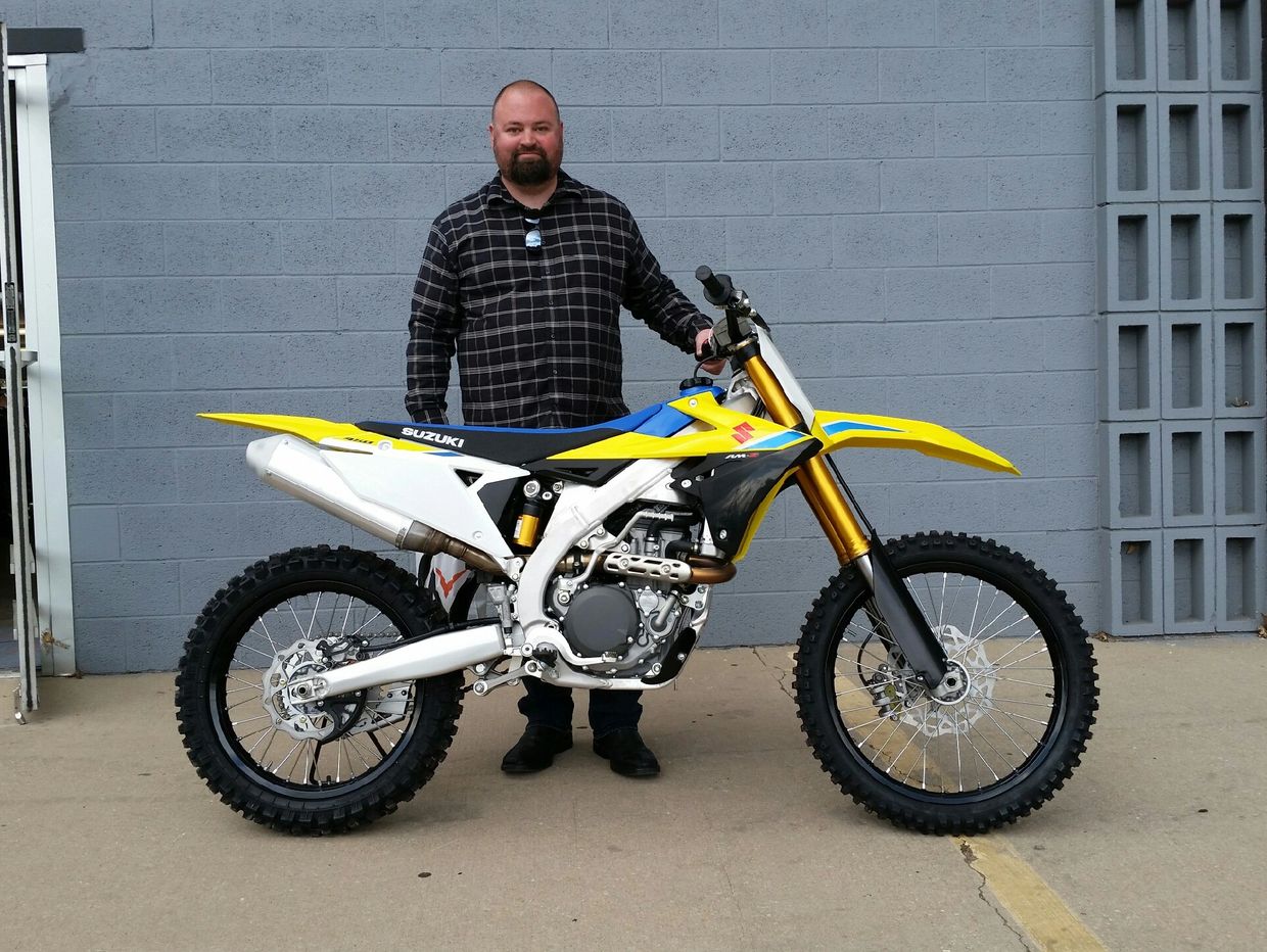 Man standing behind a yellow Suzuki dirt bike.