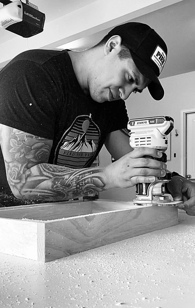 Man with tattoos using a power tool for woodworking indoors.