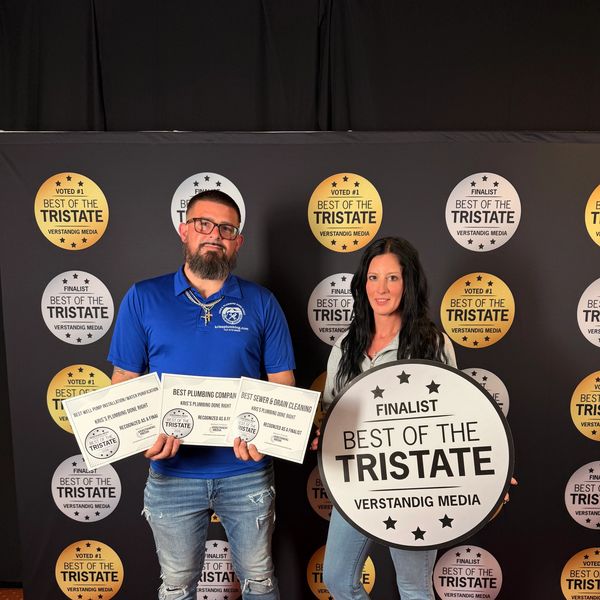Two people hold Best of the Tristate awards against a branded backdrop.company, best drain cleaning company and best well pump service company