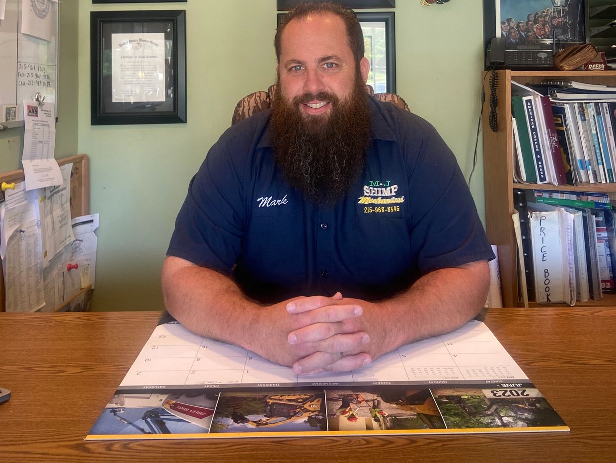 Man with a long beard sitting at a desk with a calendar.