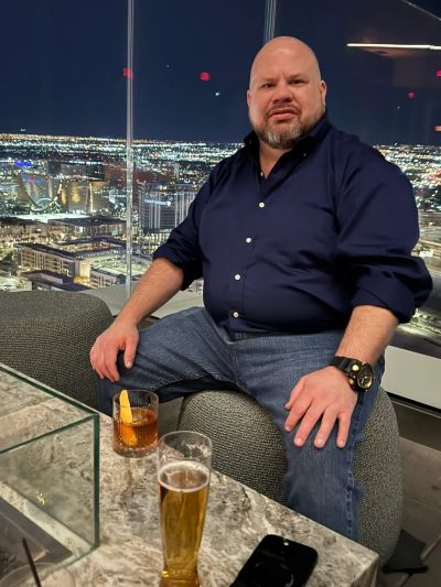 Man sitting on a chair with drinks and city lights at night.