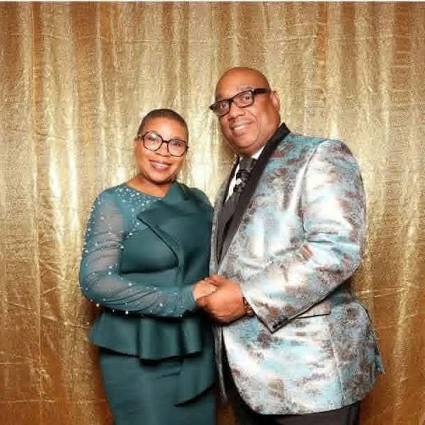 Well-dressed couple smiling against a gold backdrop.