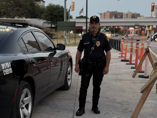 Police officer standing next to a black patrol car on a city street.