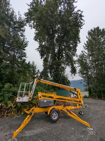 Yellow Haulotte trailer lift parked on gravel near green trees.
