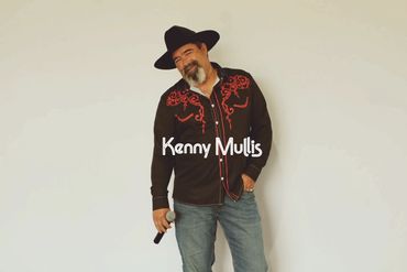 Man in cowboy hat and embroidered shirt holding a microphone, smiling.