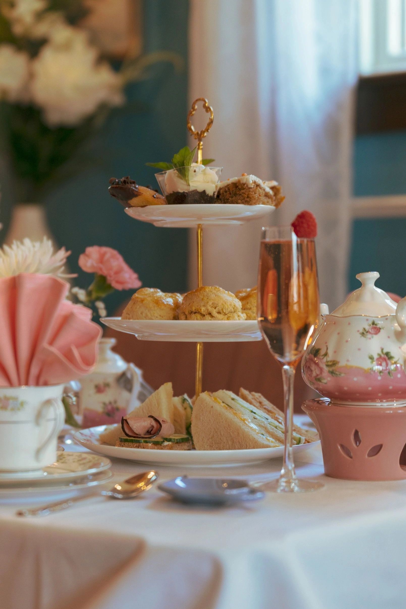 Elegant afternoon tea setup with tiered tray, sandwiches, scones, and floral teapot.
