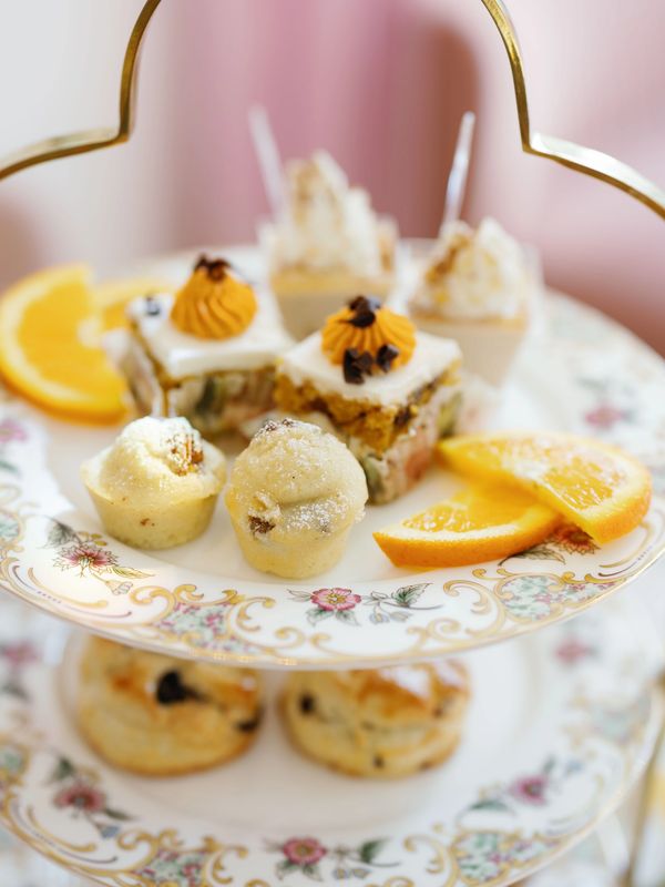 Two-tiered plate with assorted mini cakes and orange slices.