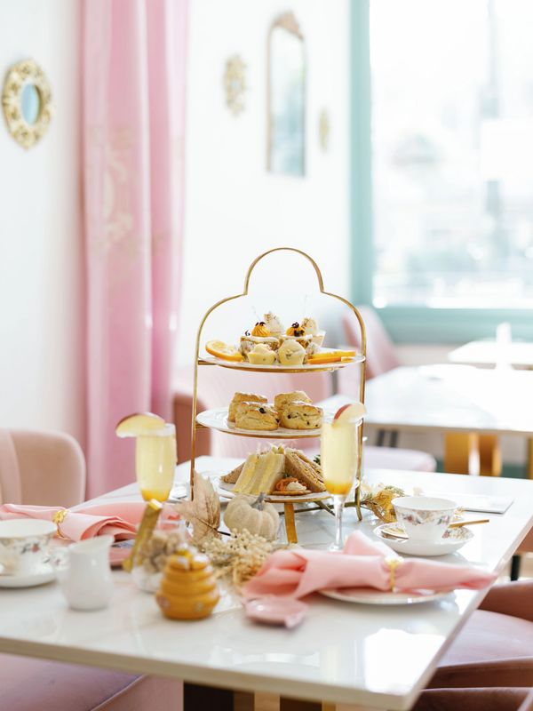 Elegant afternoon tea setup with tiered sandwiches, scones, and sweets in a pastel-themed room.
