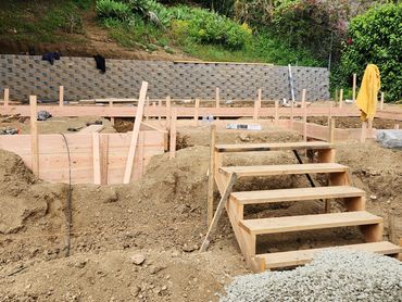 Wooden stairs and framing at a construction site with soil and stone retaining wall.