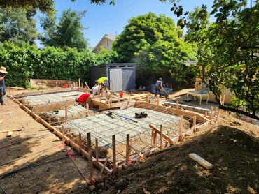Construction crew working on foundation with rebar and gravel under clear sky.