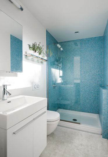 Modern bathroom with blue tiled shower and white vanity.