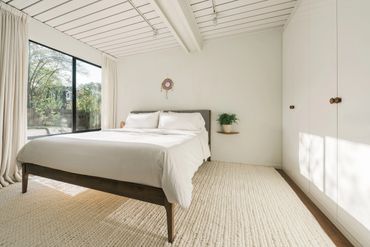 Bright minimalist bedroom with large window and cozy white bedding.