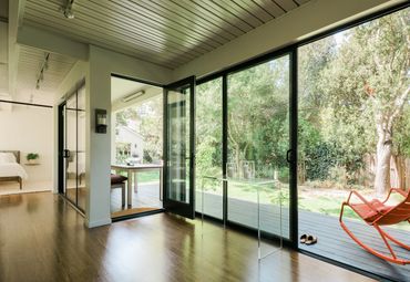 Modern home with large glass doors opening to a serene backyard with a red rocking chair.