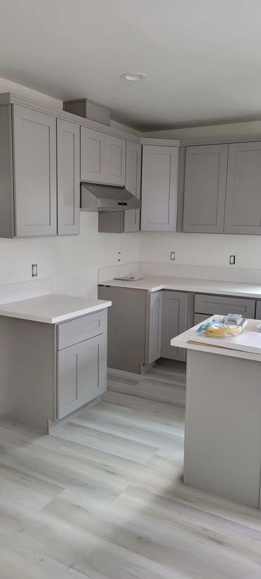 Modern kitchen with gray cabinets and light wood flooring, under construction.