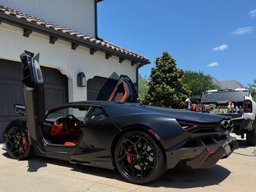 Matte black Lamborghini with scissor doors open in driveway.