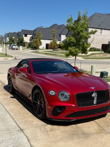 Red Bentley convertible parked in a suburban driveway on a sunny day.