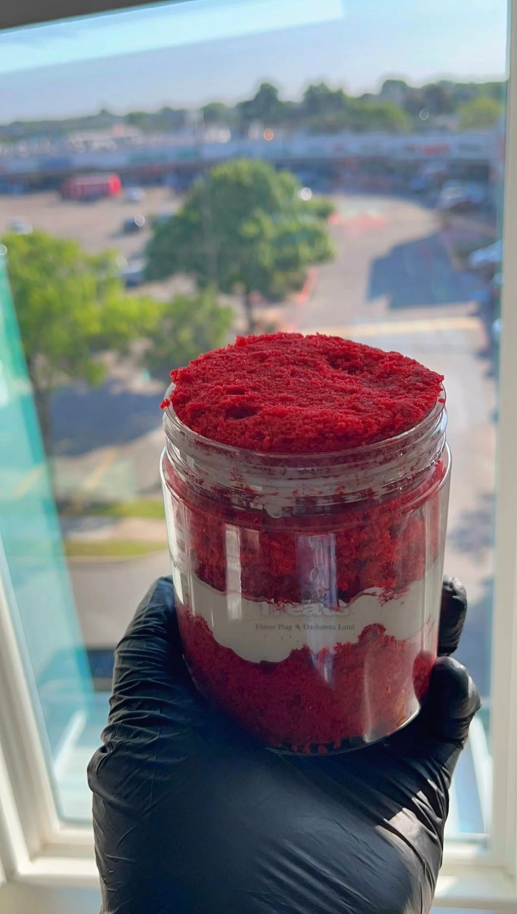 Hand holding a jar filled with layered red velvet cake and cream cheese frosting.