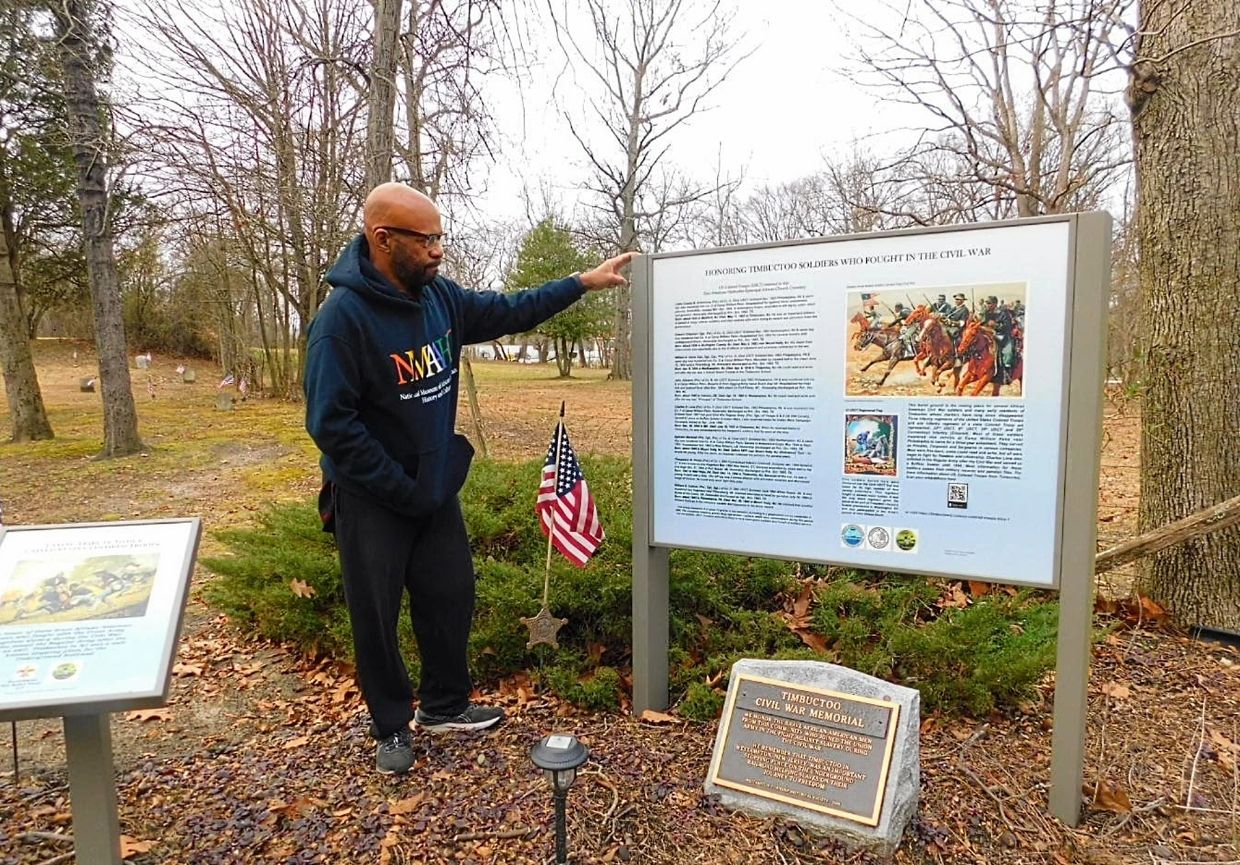 Guy Weston with sign depicting US Colored Troops (USCT) buried in the Timbuctoo cemetery
