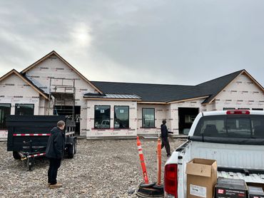 A house under construction with workers and vehicles in front.