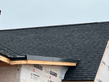 Newly installed black asphalt shingle roof on a house under construction.
