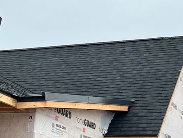 Newly installed black asphalt shingle roof on a house under construction.