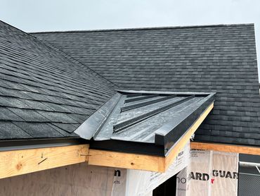 Newly constructed roof with black shingles and metal flashing.