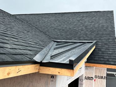 Newly constructed roof with black shingles and metal flashing.