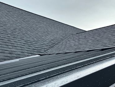 Close-up of a wet, dark gray shingled roof under a cloudy sky.