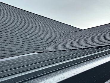 Close-up of a wet, dark gray shingled roof under a cloudy sky.