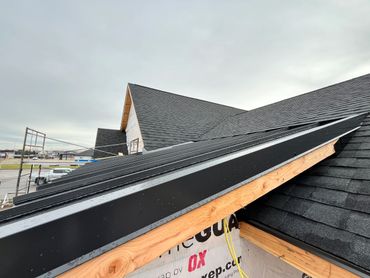 Newly installed black shingle roof on a residential building under cloudy skies.