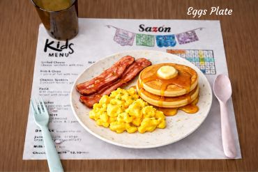 Kids' breakfast plate with scrambled eggs, bacon, pancakes, and syrup.
