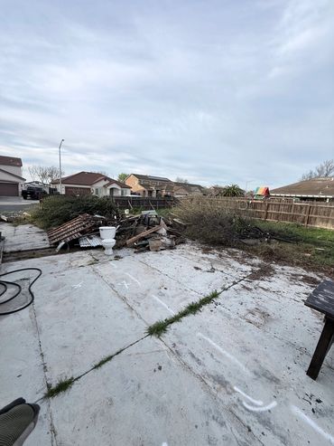 A backyard with debris and a toilet sitting on a concrete surface.