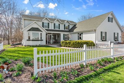 White two-story house with a manicured lawn and white picket fence on a sunny day.