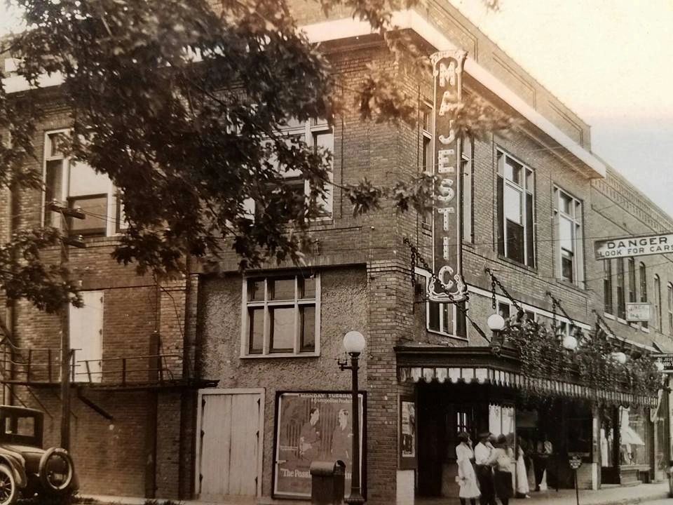 Sepia photo of Majestic Theater with old car, plants on balcony and people waiting outside.