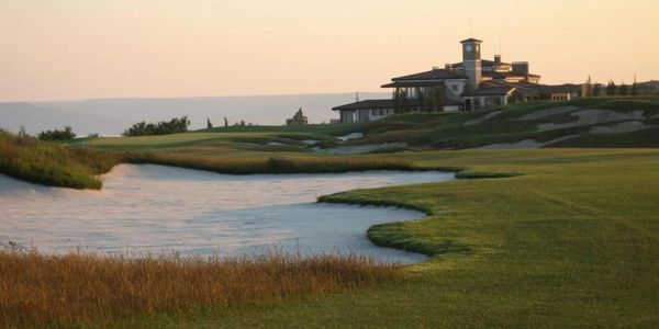 Golf course with water hazard and clubhouse at sunset.