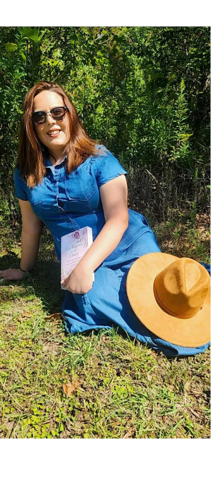 Woman in blue dress sitting on grass with a book and hat beside her.