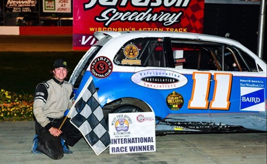 Race car driver kneels with checkered flag beside winning car number 11.