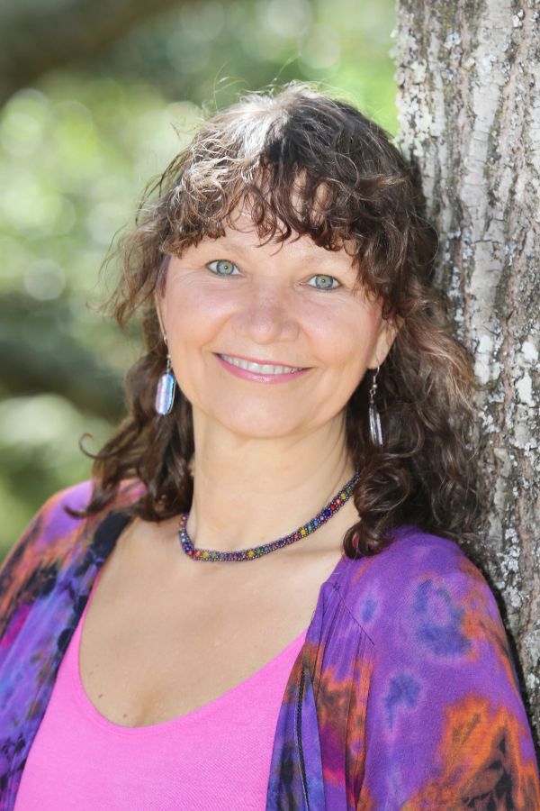 Smiling woman wearing colorful clothes leaning against a tree.