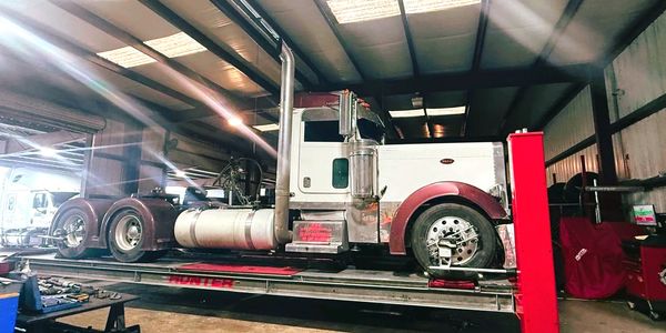 A semi truck on a lift inside a maintenance garage with tools scattered around.