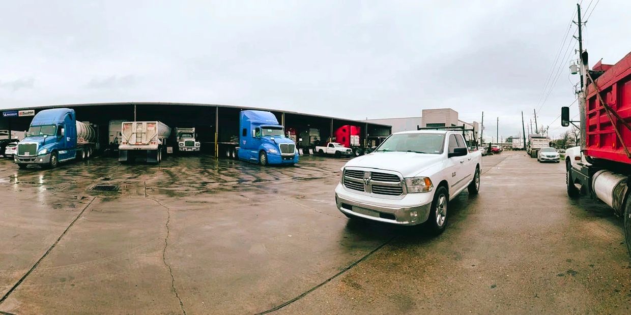A parking area with trucks and a white pickup on a wet concrete surface.