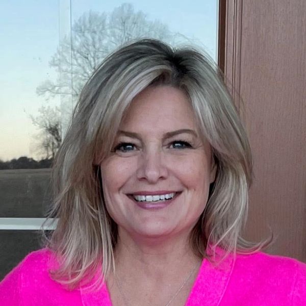 Smiling woman with blonde hair in a bright pink top.