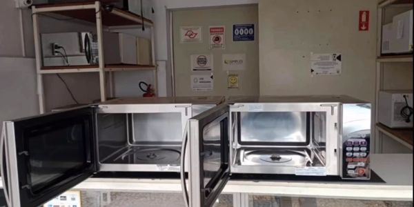 Two open microwave ovens on a white table in a room with shelves.